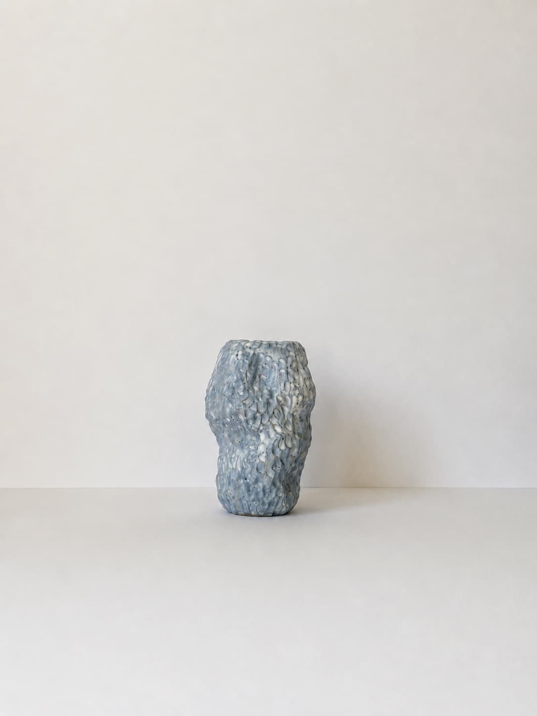 A small blue and white CLÆY vase standing against a pale wall