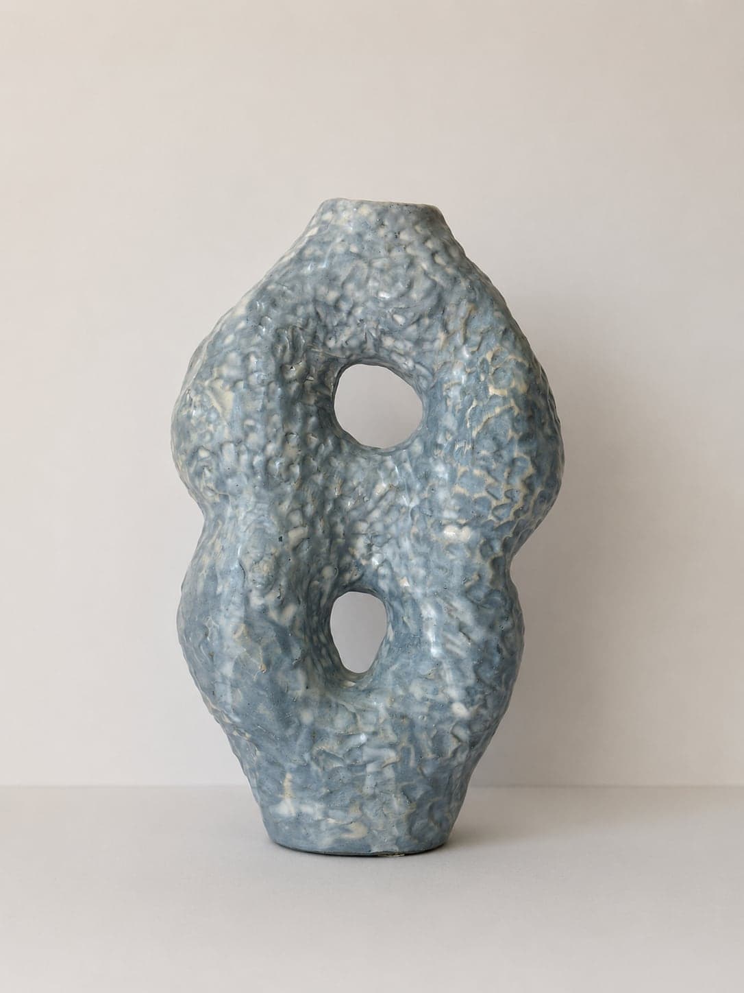 A blue-glazed CLÆY vessel with two openings, standing against a plain wall